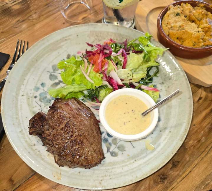 Steak grillé accompagné d'une salade mixte, d'une sauce crémeuse et d'une portion d'écrasé de pommes de terre Valergues